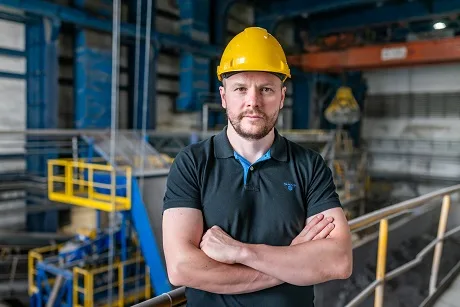 Muž v žluté helmetě stojí na průmyslovém pracovišti.