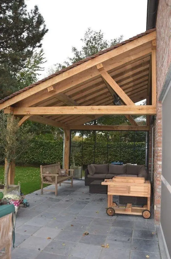 Dřevěná pergola u domu s pohovkou a skleněnými panely.