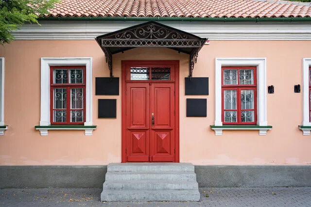 Černá kovová stříška nad červenými dveřmi s ozdobným motivem.