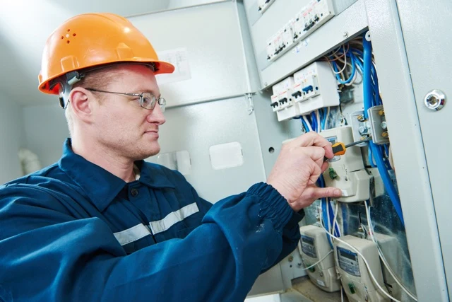 Elektrikář upravuje komponenty v průmyslovém elektrickém rozvaděči.