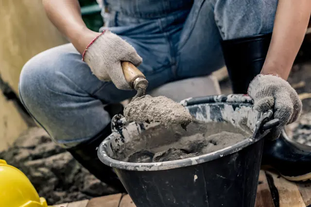 Stavebník míchá beton lopatkou z kbelíku.