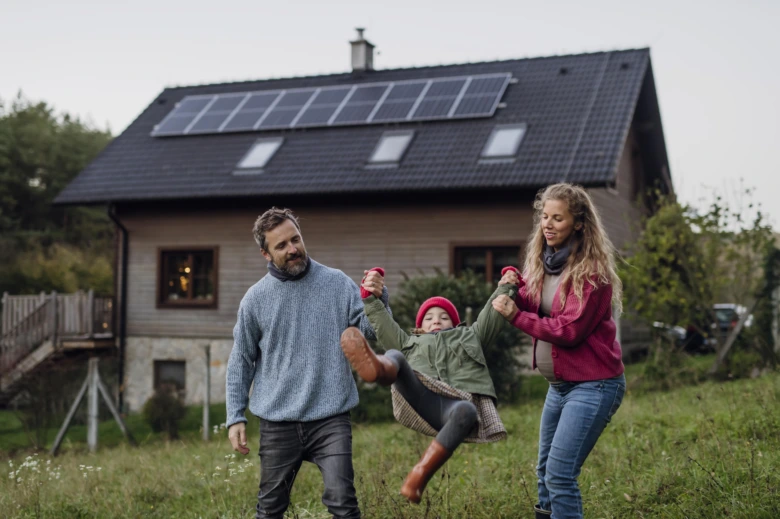 Rodina hraje před domem s fotovoltaickými panely na střechě.
