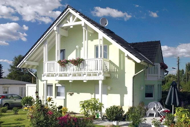 Dřevostavba na klíč s balkónem a zahradou pod modrou oblohou.