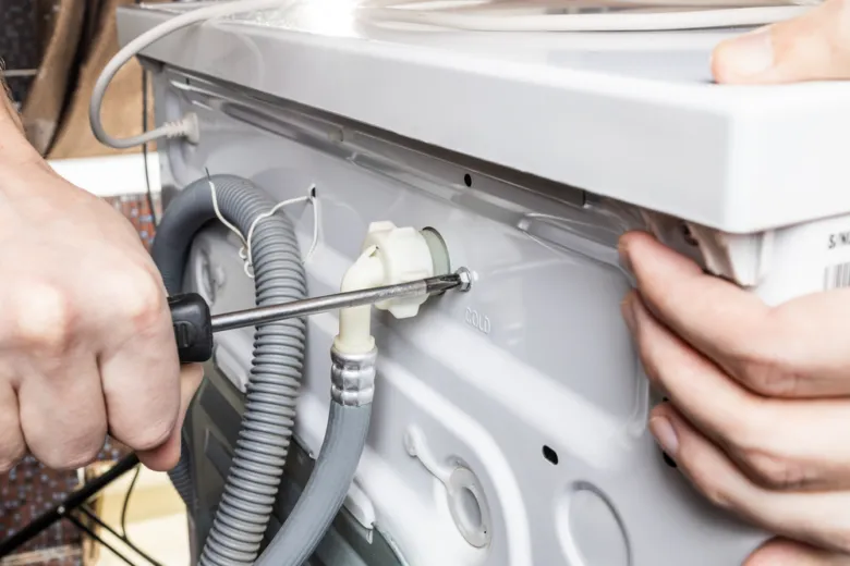 Mechanik opravuje myčku odstraňováním zadního krytu šroubovákem.