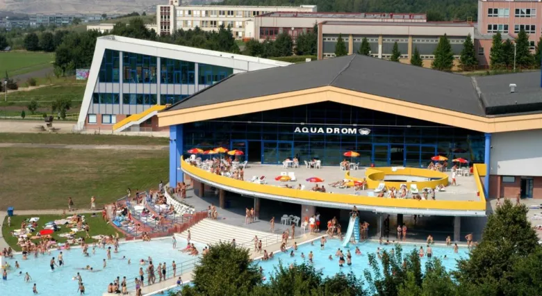 Vnější pohled na bazénový komplex Aquadrom v Mostě s lidmi ve vodě.