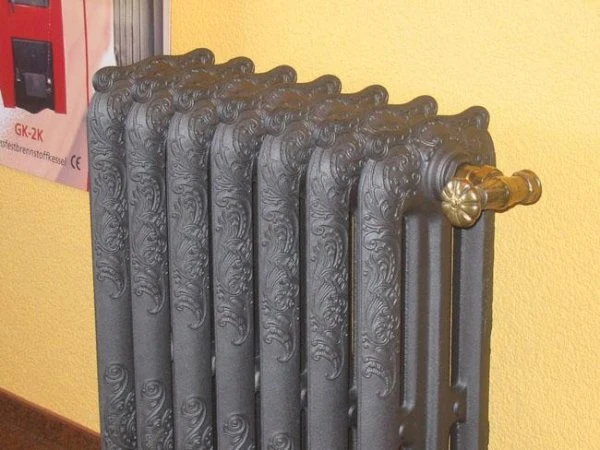Litinový radiátor s dekorativním vzorem na žluté zdi.