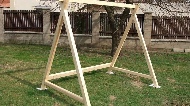 Dřevěná konstrukce houpačky na zahradu před plotem.