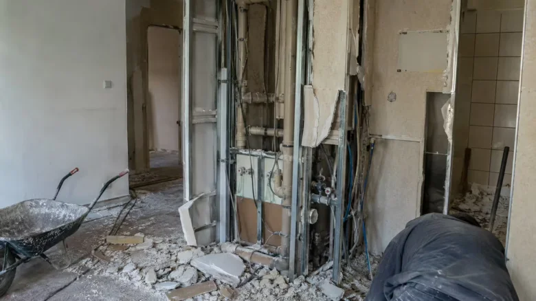 Byt v rekonstrukci s odhalenými instalacemi a odpady na zemi.