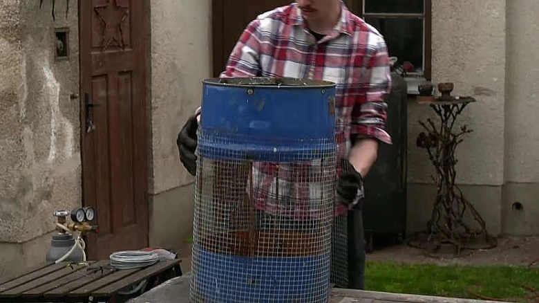 Muž drží modrou barel síto na prosévání zeminy.