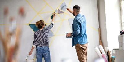 Muž a žena malují geometrické vzory na bílou stěnu.