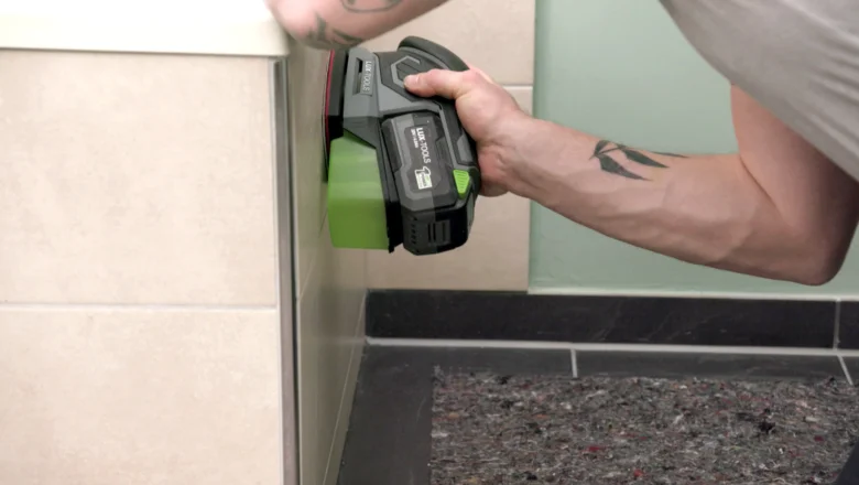 Muž čistí fugy na dlažbě v koupelně elektrickým nástrojem.