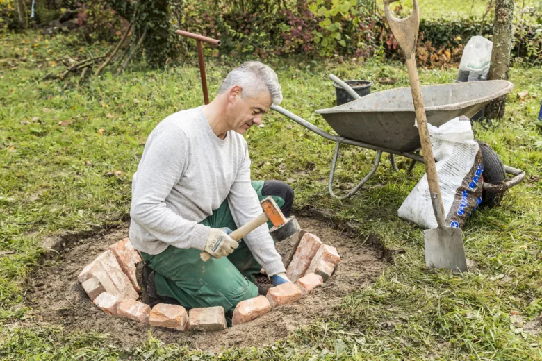 Muž staví kamenné ohniště z cihel na trávníku