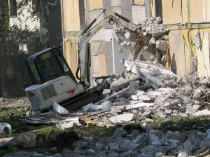 Bílý bagr rozebírá budovu na místě stavebních prací.