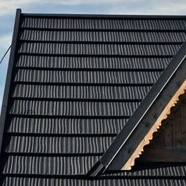 Detail tmavých plechových střešní krytin s hřebenem.