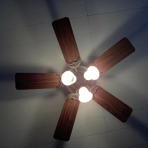 Stropní ventilátor s dřevěnými lopatkami a třemi svítícími žárovkami.