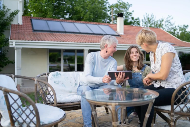 Rodina sedí venku u domu s fotovoltaickými panely na střeše.