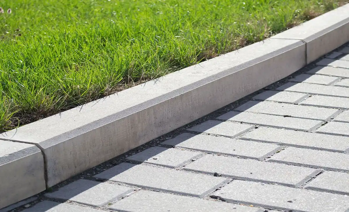 Betonový obrubník oddělující trávník od dlažby na chodníku.