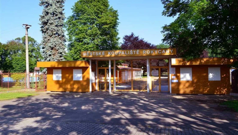 Vstup do městského bazénu v Rokycanách s oranžovou budovou.