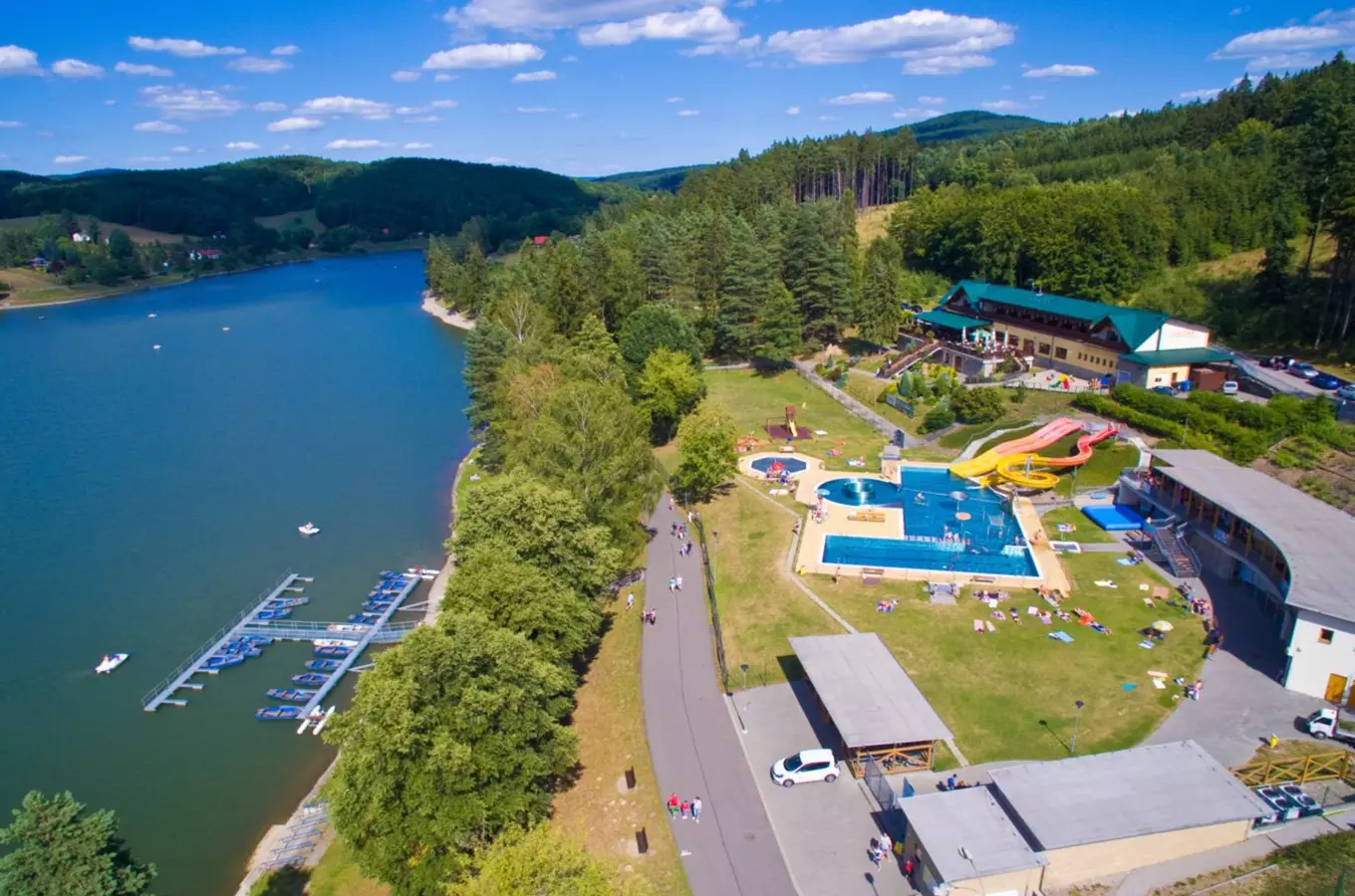 Pohled na aquapark s bazénem a skluzavkami u jezera.