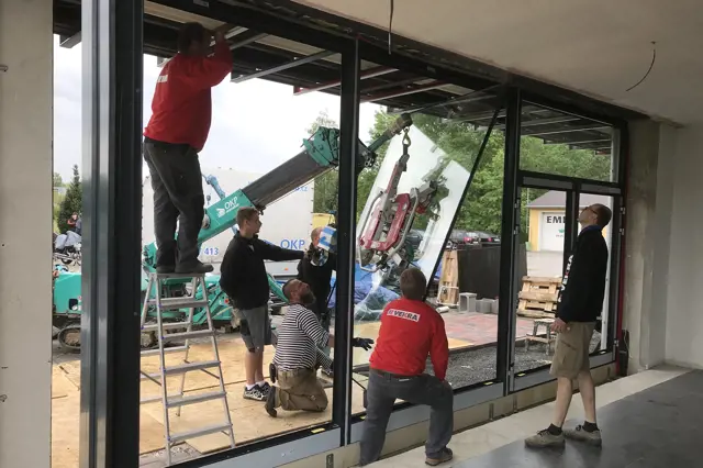 Práce na instalaci velkých oken v domě s pomocí techniky.