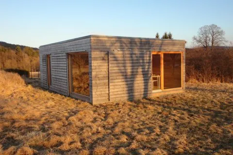 Moderní prefabrikovaný dřevěný dům stojí na travnatém poli.