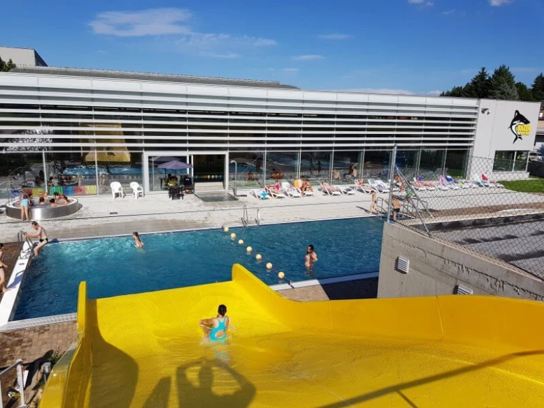 Venkovní bazén v nové Pace s žlutou vodní skluzavkou.