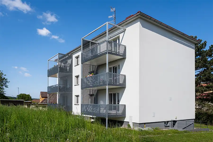 Moderní balkony s kovovými mřížemi na bílém bytovém domě.
