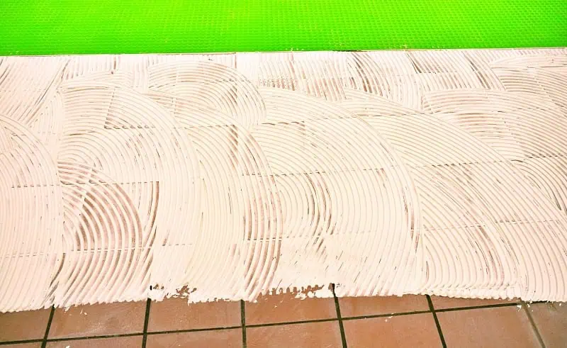 Bílá lepidlo pro dlažbu rozetřené na podlahu před pokládkou.