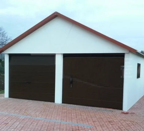 Bílá omítnutá garáž s dvěma hnědými bránami na dlažbě.