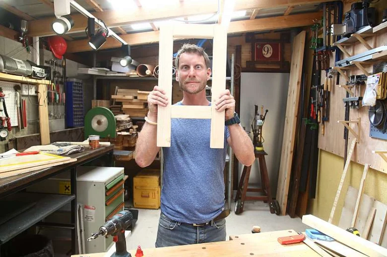 Muž drží dřevěný rám v dílně na stavbu botníku.