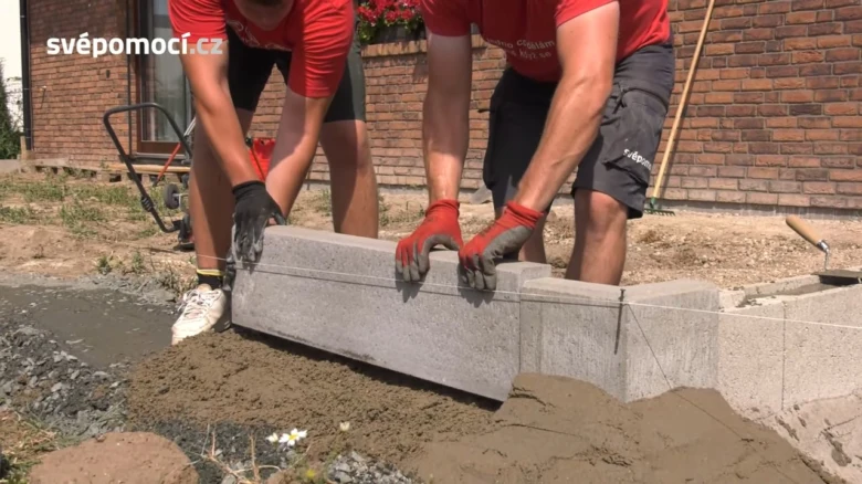 Muži pokládají betonový obrubník na čerstvou maltu.
