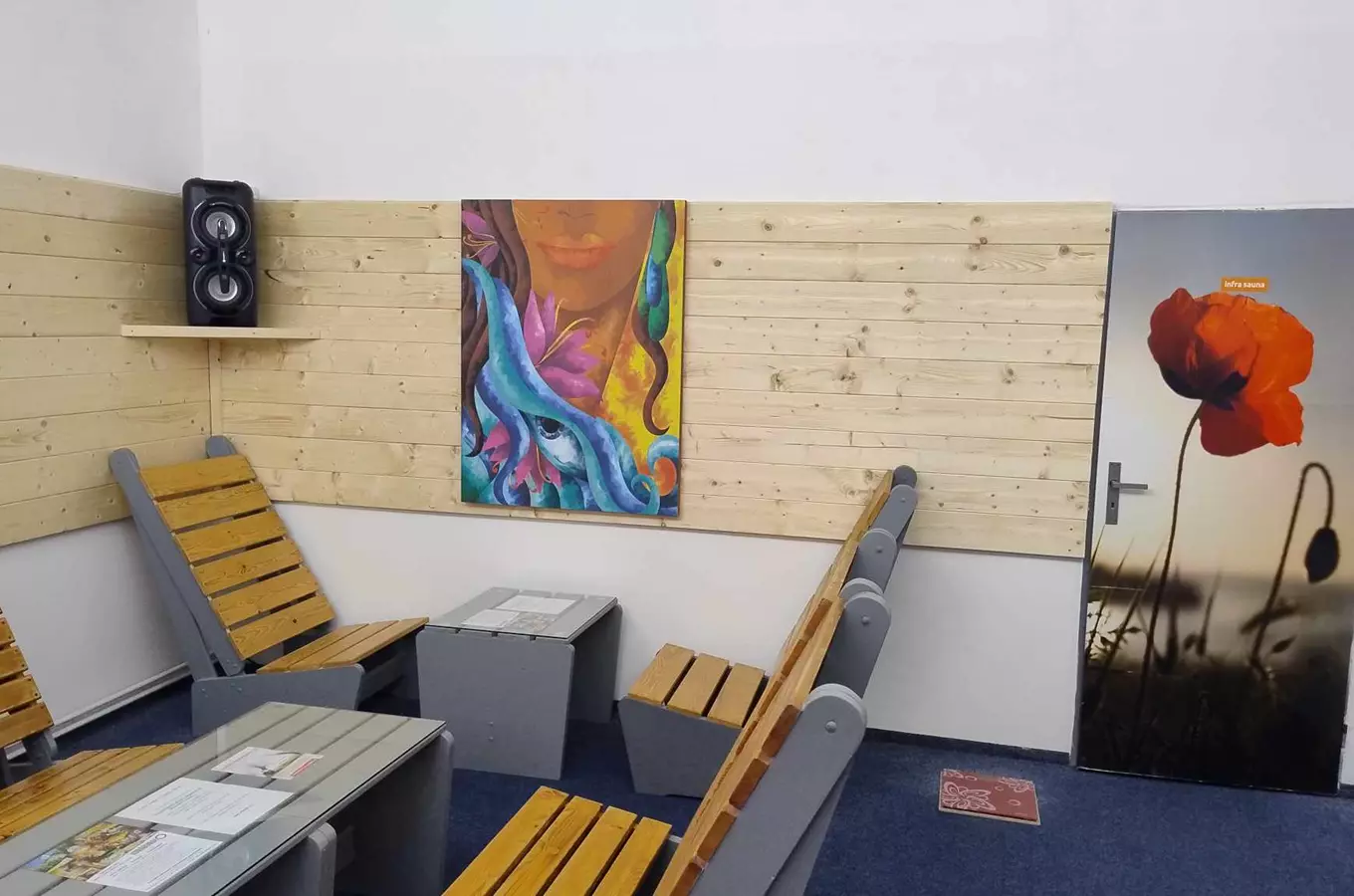 Modern interiér sauny s dřevěnými židlemi a barevnou malbou na zdi.