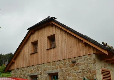Dům s provětrávanou fasádou z dřevěného obkladu a kamenného základu.