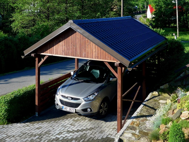 Stříbrný automobil pod dřevěným přístřeškem s modrou střechou.