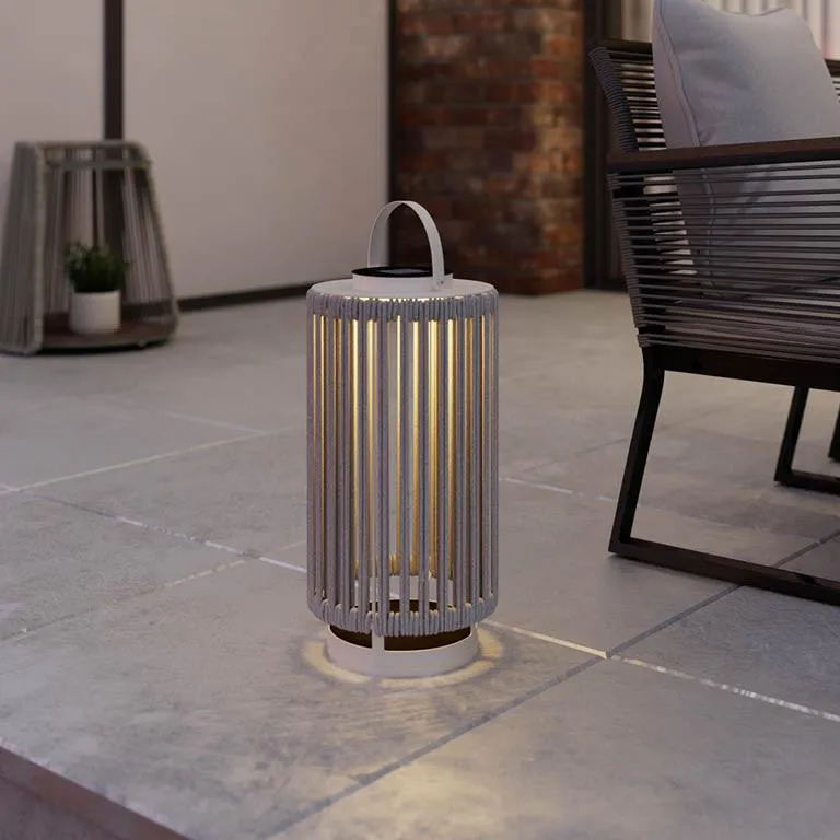Venkovní lampa na dlažbě terasy u zahradního nábytku.