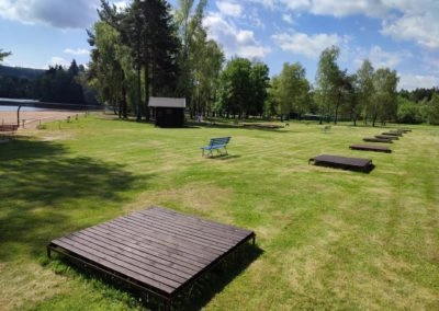 Venkovní koupaliště s dřevěnými plošinami a lavičkou