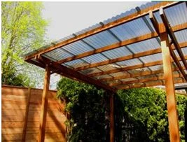 Dřevěná pergola s průsvitnou střechou v zahradním prostředí.