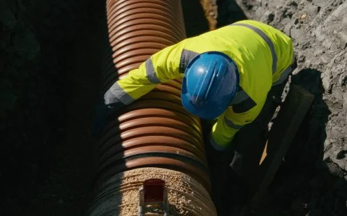 Montáž velkého drenážního potrubí pracovníkem na staveništi.