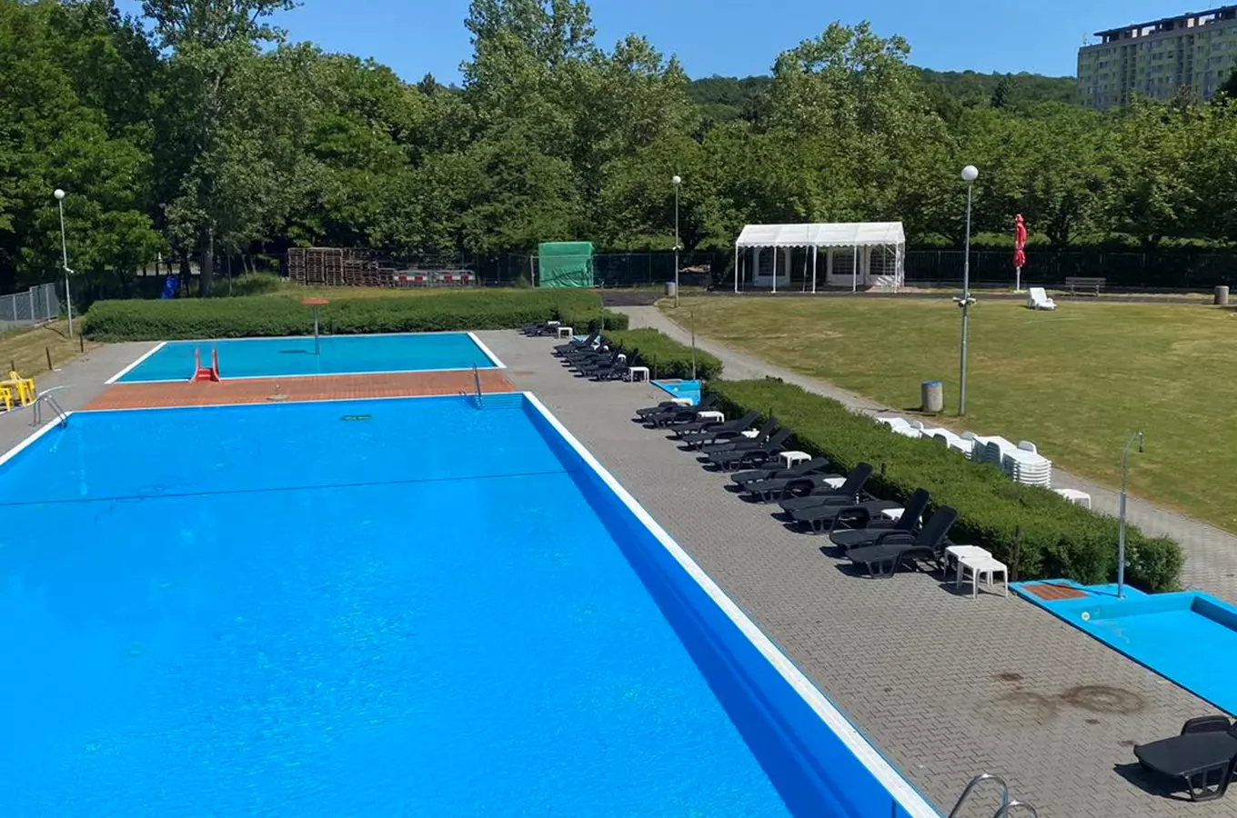 Venkovní bazén v Ládví s lehátky a trávníkem.