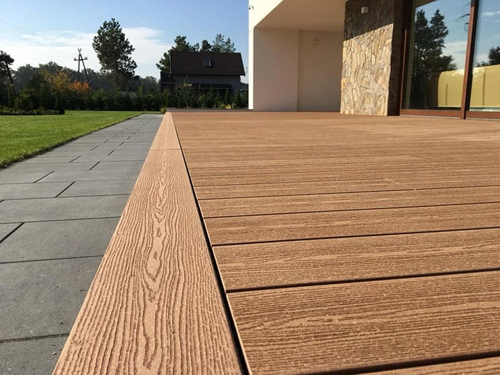 Moderní dřevěná terasa s kompozitovými prkny vedle dlažby.