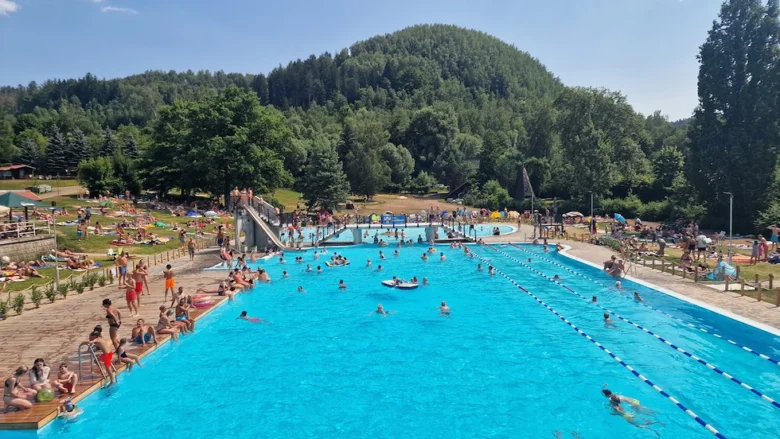 Venkovní bazén v Košťálově s plavci a okolními lesy.