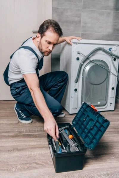 Technik opravuje pračku s nářadím v krabici.