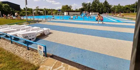 Venkovní plavecký bazén s modrou dlažbou a lehátky.