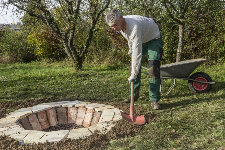 Muž staví ohniště z cihel v zahradě.