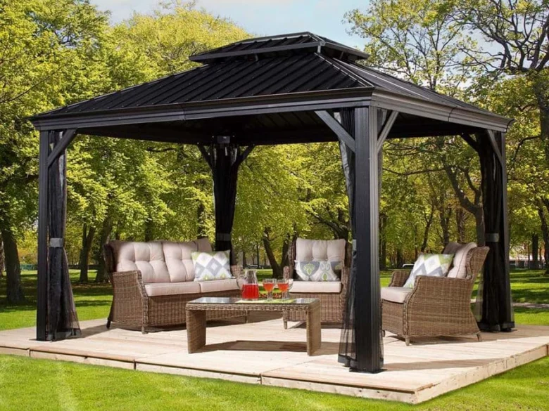 Černá zahradní pergola s nábytkem na dřevěné terase uprostřed zelené trávy.