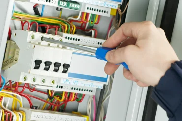 Elektrikář upravuje spoje v rozvaděči šroubovákem.