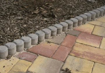 Betonové obrubníky položené vedle dlažebního chodníku s dřevitým substrátem.