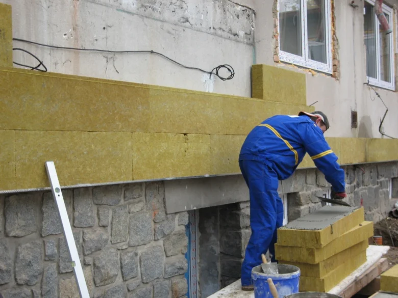 Stavebník montuje žluté minerální vlnové desky na fasádu domu.