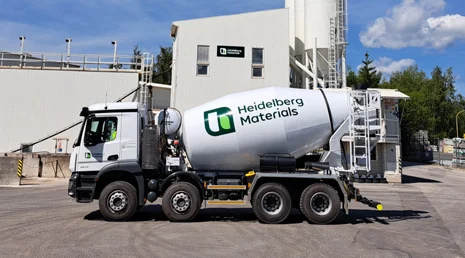 Bílý betonový míchač značky Heidelberg Materials před továrnou.