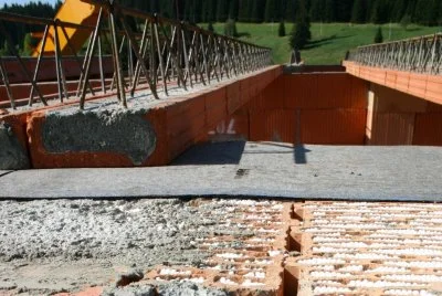 Částečně postavený ocelový most s betonovými opěrami na pozadí zelených kopců.